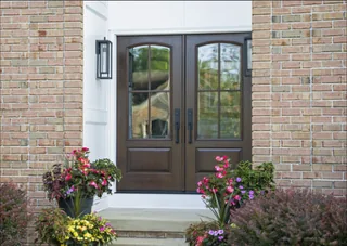 Dark stained arched double entry doors with glass on a brick home