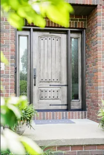 Rustic grey entry door with sidelights on a brick home