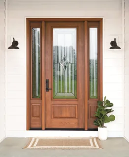 Light wood entry door with decorative glass and sidelights on white siding