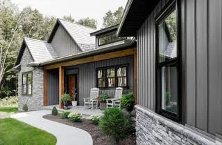 Grey board-and-batten home with stone accents and black windows